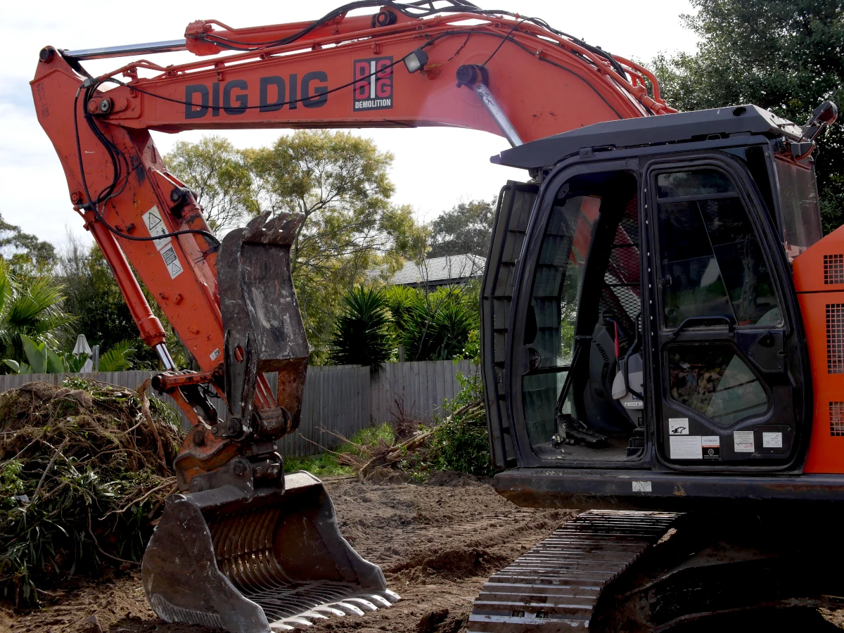 Dig Dig excavator with grab attachment clearing garden waste on a residential block
